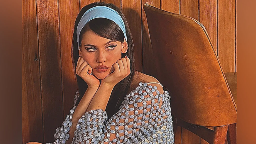 הזמרת סיינה ספירו (Sienna Spiro) בתמונת קידום לאלבום הבכורה, יושבת שעונה על ידיה עם סרט תכלת בשיער